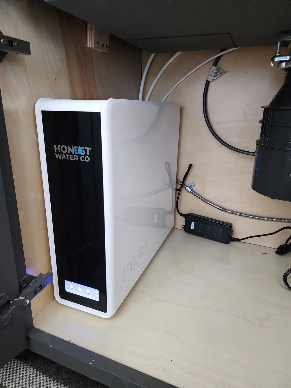 Tankless reverse osmosis system mounted under a kitchen sink beside the disposal