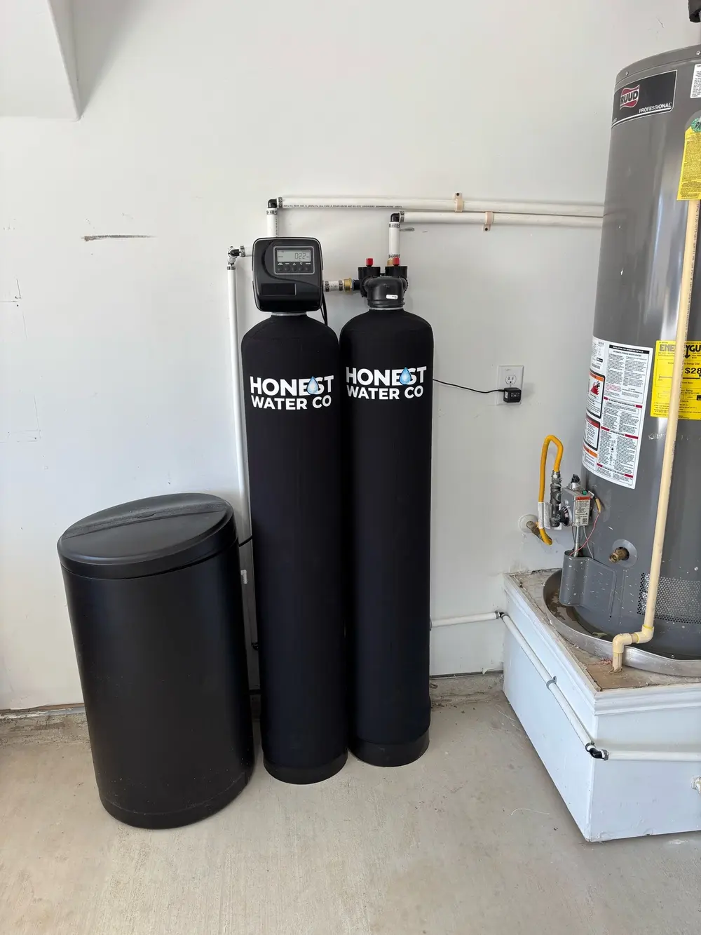 Two branded filtration tanks and a round brine tank installed next to a gas water heater